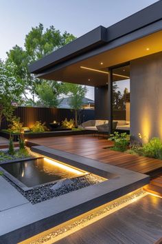 a modern house with wooden decking and water feature in the front yard at dusk