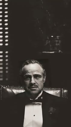 a black and white photo of a man in a tuxedo sitting in a chair