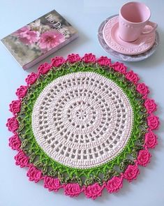 a crocheted doily sits on a table next to a pink cup and saucer