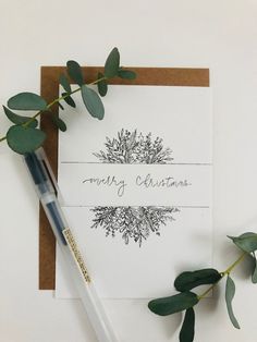 a card with the words merry christmas written on it next to a pen and eucalyptus leaves