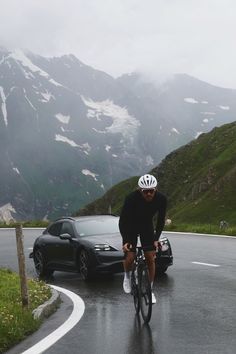 a man riding a bike down the middle of a road next to a black car