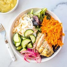 a salad with chicken, cucumbers, onions and cheese in a white bowl