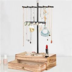 a jewelry stand with necklaces, earrings and lipstick on it in front of a white wall