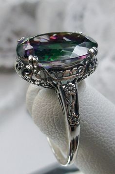 Natural Rainbow Mystic Topaz White Gold Ring Edward Design#70 Custom Here we have an Edwardian reproduction ring in 10K or 14K white gold filigree with a stunning Natural Rainbow Mystic Topaz gemstone solitaire. This full cut oval Topaz is 14mm in length and 10mm in width. This ring also sits 7mm off the finger. The inside of the band is marked 10K or 14K for gold, and can be engraved at request. Notice the beautiful leaf design of the gold filigree setting and etched band. This is a lovely rend Elegant Iridescent Topaz Gemstone Ring, Elegant Iridescent Rings With Accent Stones, Vintage Iridescent Rings For Wedding, Elegant Iridescent Topaz Ring For Anniversary, Iridescent Topaz Ring For Anniversary, Elegant Iridescent Rings For Formal Occasions, Elegant Iridescent Round Topaz Ring, Mystic Topaz Ring, Luxury Rings