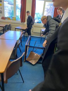 a group of men standing around a wooden table in a room filled with desks