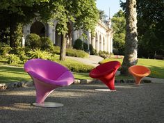 three different colored chairs sitting in the middle of a park