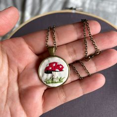 a hand holding a small pendant with a red mushroom on it's front and back