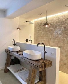 two white sinks sitting on top of a wooden bench in a bathroom next to a brick wall