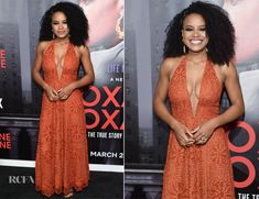 a woman in an orange dress standing on a black carpet and smiling at the camera