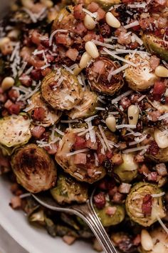 a white bowl filled with brussel sprouts, bacon and pine nuts