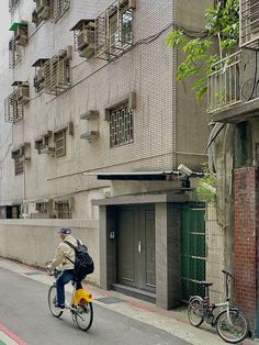 a person riding a bike down the street in front of a tall building with balconies