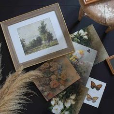 some pictures are laying on the floor next to a chair and flowers, with a butterfly flying over them