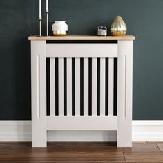 a white side table with candles on it in front of a green wall and wooden floor