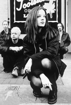 black and white photograph of woman sitting on the sidewalk with other people standing around her