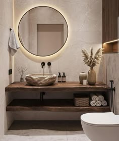 a white toilet sitting next to a bathroom sink under a round mirror above a wooden counter