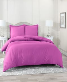 a bed with pink sheets and pillows in a white room next to a lamp on the floor