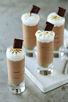 four desserts with chocolate and whipped cream in them on a white tray next to silverware