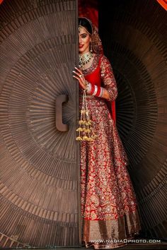 a woman in a red and gold bridal outfit holding a golden bell on her hand