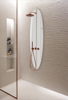 an oval mirror hanging on the wall next to a shower head and faucet