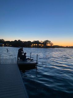 a man sitting on a dock next to a body of water at sunset or dawn