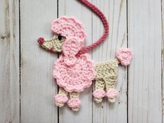 a crocheted poodle ornament hanging on a white wooden background with pink yarn