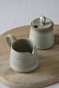 two ceramic containers sitting on top of a wooden tray