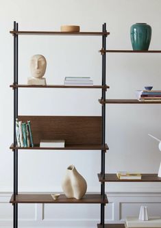 a shelf with books and vases on it in a room that has white walls