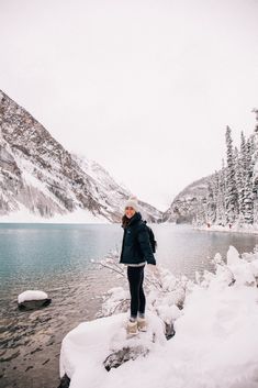 a woman standing on top of a snow covered rock next to a lake