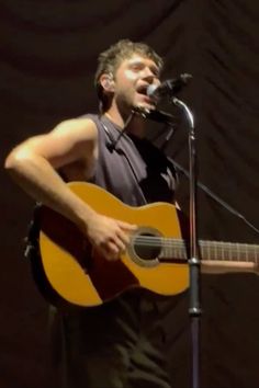 a man singing into a microphone while holding an acoustic guitar