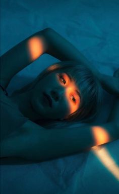 a woman laying on top of a bed under a blue blanket with light shining through her eyes