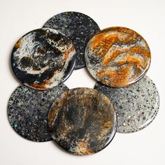 four different colored marbles are arranged on a white surface with black and orange speckles