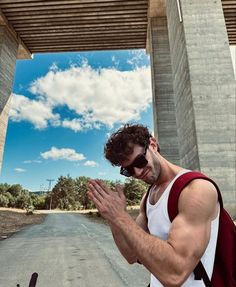 a man standing on the side of a road holding his hands together while wearing sunglasses