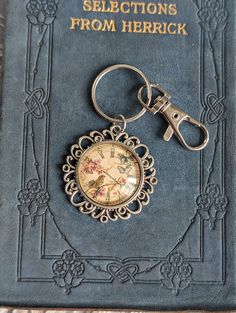 an antique pocket watch keychain is sitting on top of a book with the title selections from herrick