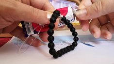 two hands are making a beaded bracelet out of black beads and some glue on it