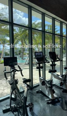 there are many exercise bikes in the gym with large windows looking out onto the pool