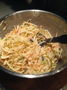 a silver bowl filled with coleslaw on top of a wooden table next to a black spatula