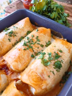 an enchilada dish in a blue casserole dish with tomatoes and parsley