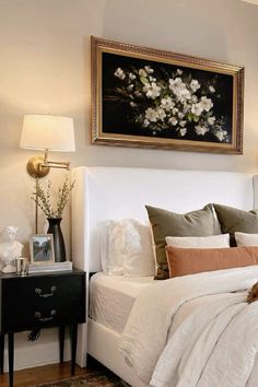 a bed with white sheets and pillows next to a painting on the wall above it