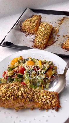 a white plate topped with food next to a pan filled with breaded fish and vegetables