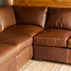 a large brown leather couch sitting on top of a wooden floor next to a wall