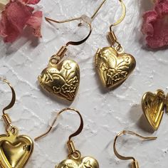 Elevate your style with our Gold Heart Locket Earrings, a delightful blend of charm and elegance. Each earring showcases a heart-shaped locket with an intricate floral design, infusing your look with a touch of romance and a delicate, feminine aesthetic. Crafted with nickel-free earring posts, these earrings prioritize comfort and safety, making them the perfect choice for any occasion. Embrace beauty and sophistication with these exquisite accessories. Metal Heart Pendant Earrings For Gift, Heart Charm Metal Earrings For Gift, Vintage Heart Charm Earrings For Valentine's Day, Metal Heart Earrings For Wedding, Heart-shaped Metal Earrings For Wedding, Metal Heart Earrings With Matching Pair For Wedding, Dainty Metal Earrings For Valentine's Day, Vintage Metal Heart Earrings For Valentine's Day, Metal Open Heart Earrings For Gift