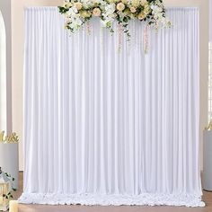 a white backdrop with flowers and candles in front of the curtain for a wedding ceremony