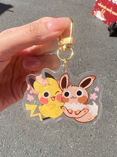 a hand holding a pokemon keychain with pikachu and eebi on it