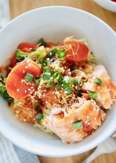 a white bowl filled with noodles and vegetables on top of a wooden table next to a fork