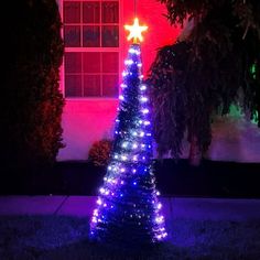 a lighted christmas tree in front of a house at night with red and blue lights