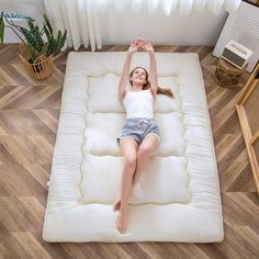 a woman laying on top of a mattress in the middle of a room with wooden floors