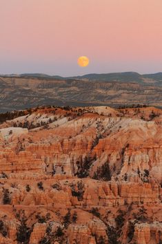 the full moon is setting in the sky over some hills and trees on top of them