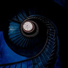 a spiral staircase with a clock in the center and blue walls behind it at night