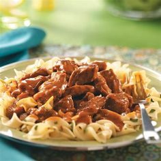 a white plate topped with pasta and meat covered in gravy on top of a table