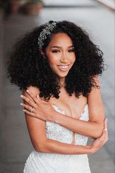 a woman with curly hair wearing a tiara and smiling at the camera while standing in front of a building